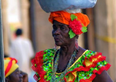 Kobieta w kolorowym stroju z miską owoców na głowie